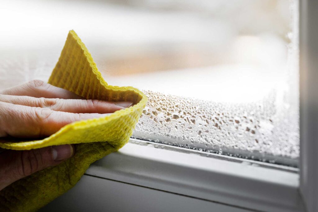 woman wiping condensation from window sill